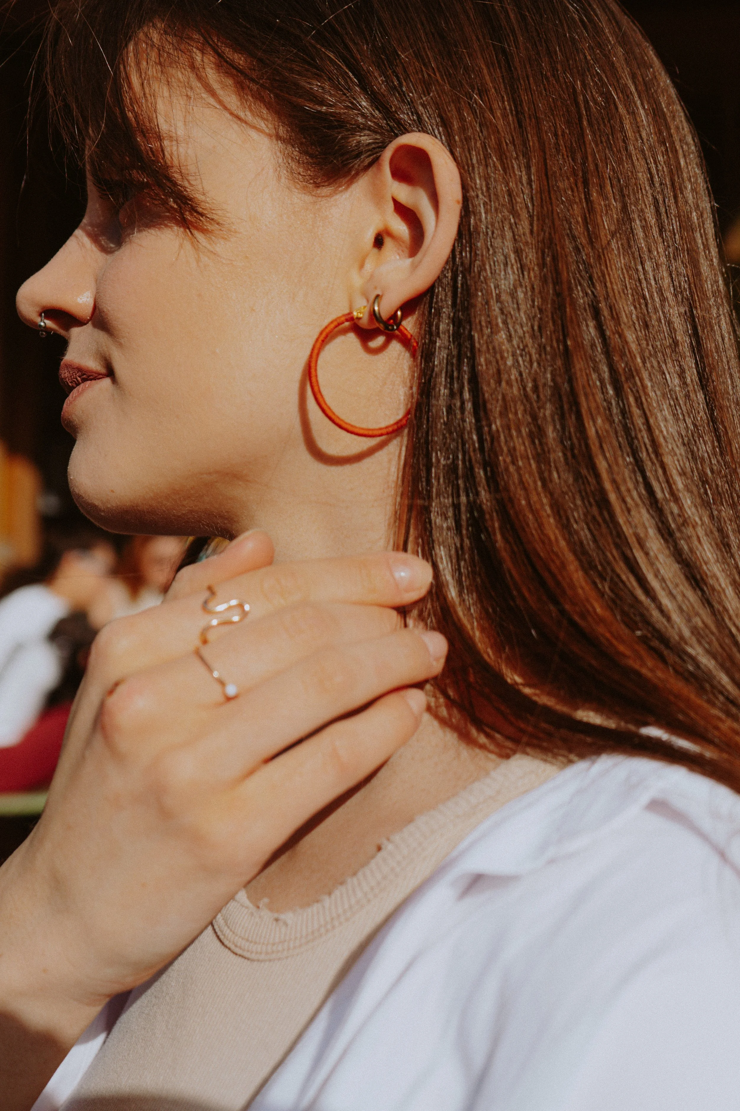 Close-up side profile of a woman's face, ear with gold hoop earring, hand with rings near her neck, and reddish-brown hair.