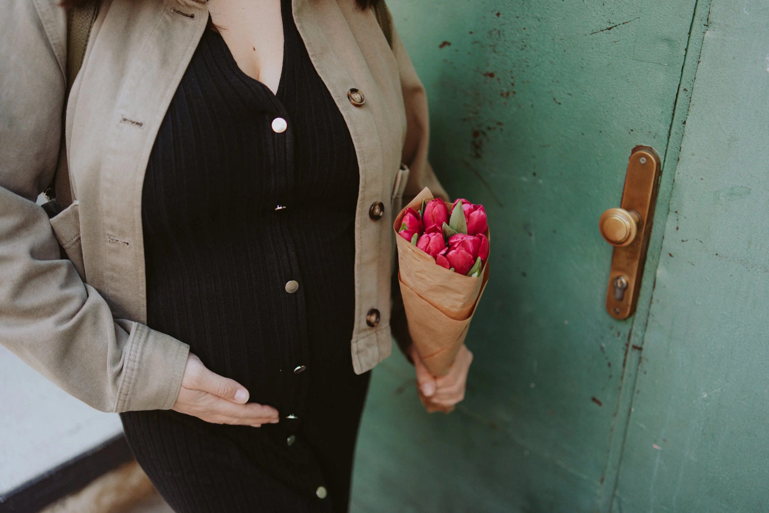 A person holding a bouquet of pink tulips standing near a green door with a brass handle.