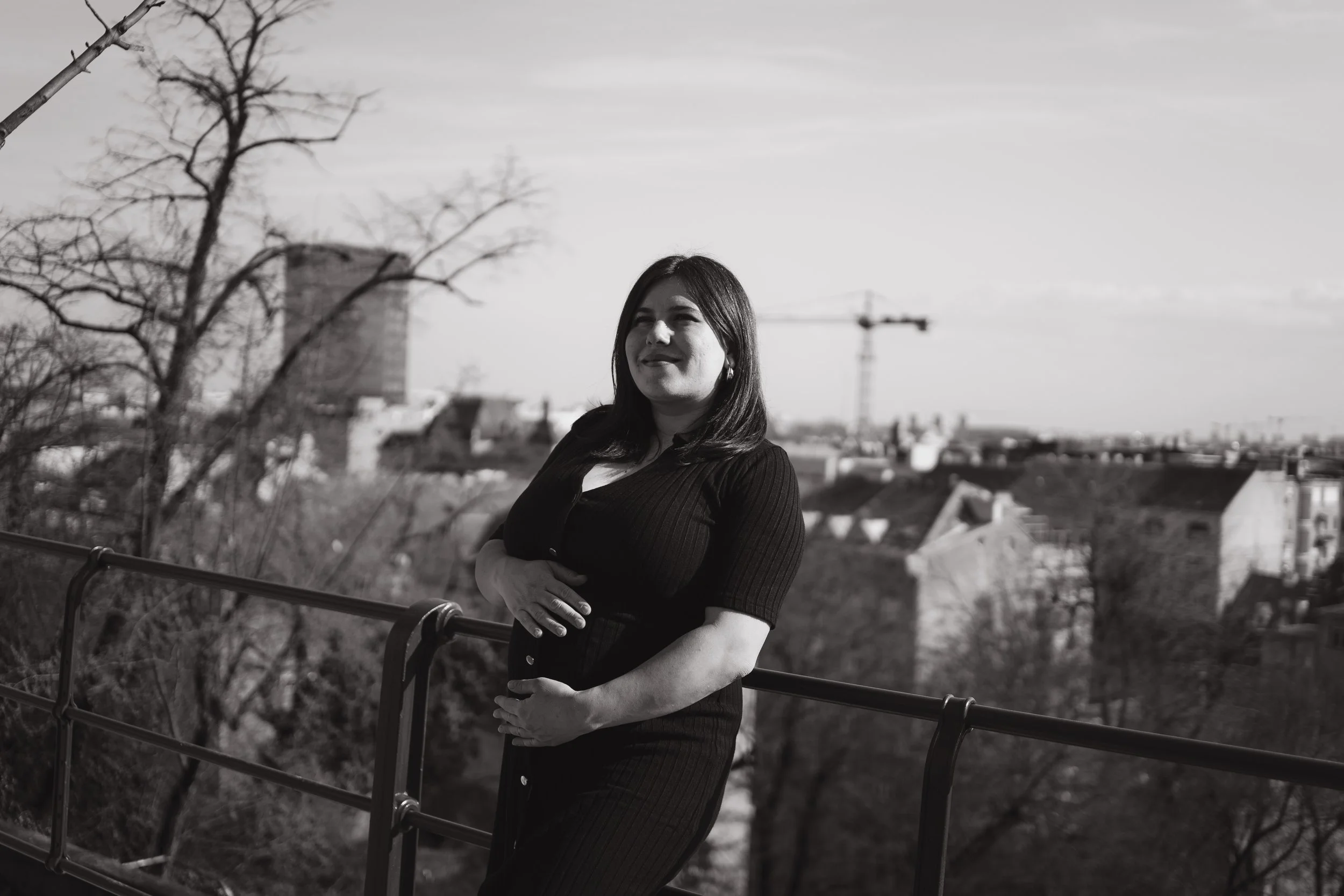 A woman with dark hair wearing a black dress standing outdoors on a rooftop with a cityscape in the background, black and white photo.