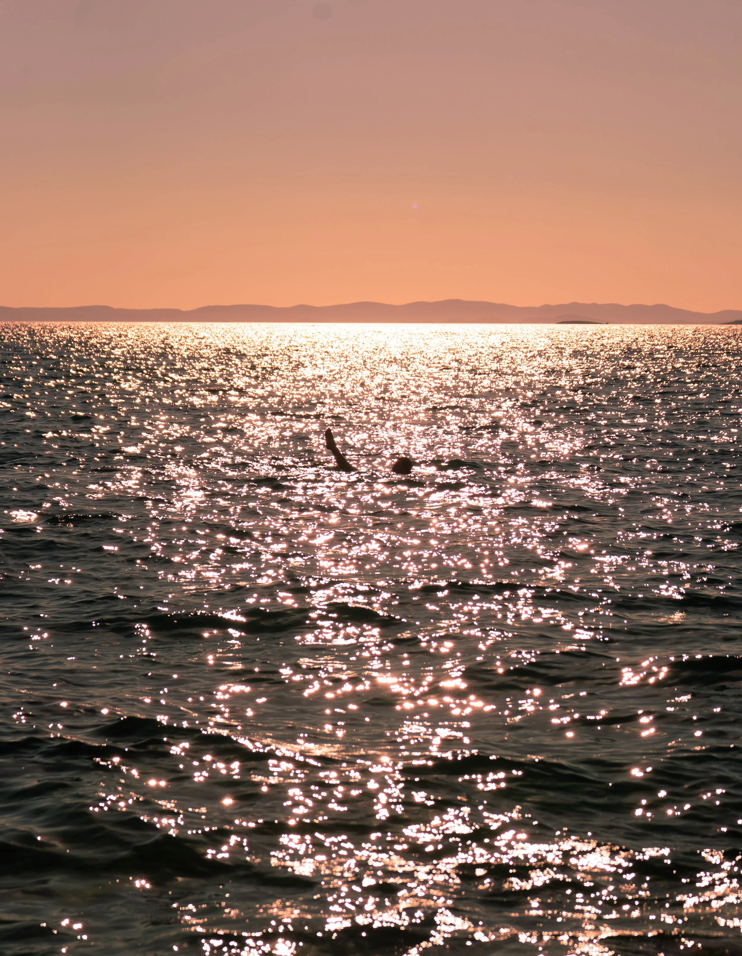 Dreamy sunset over a body of water with shimmering reflections and distant mountains.