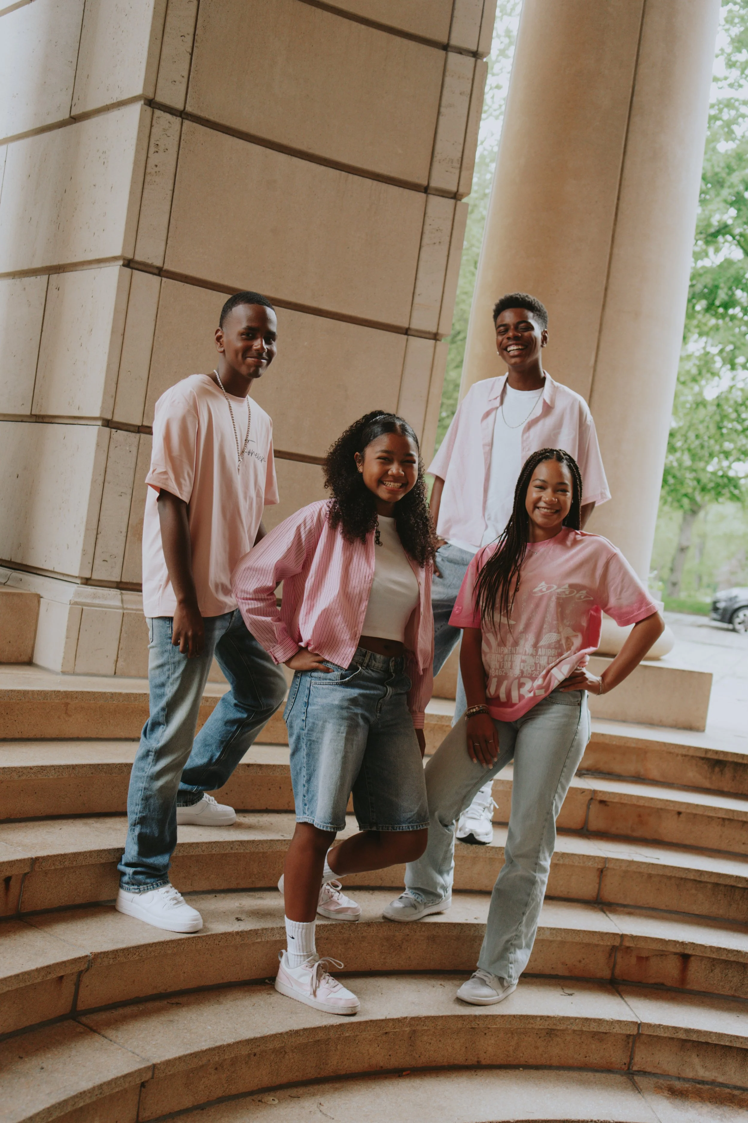 Group of five young people standing on stairs outside near large columns, smiling and posing for a photo.