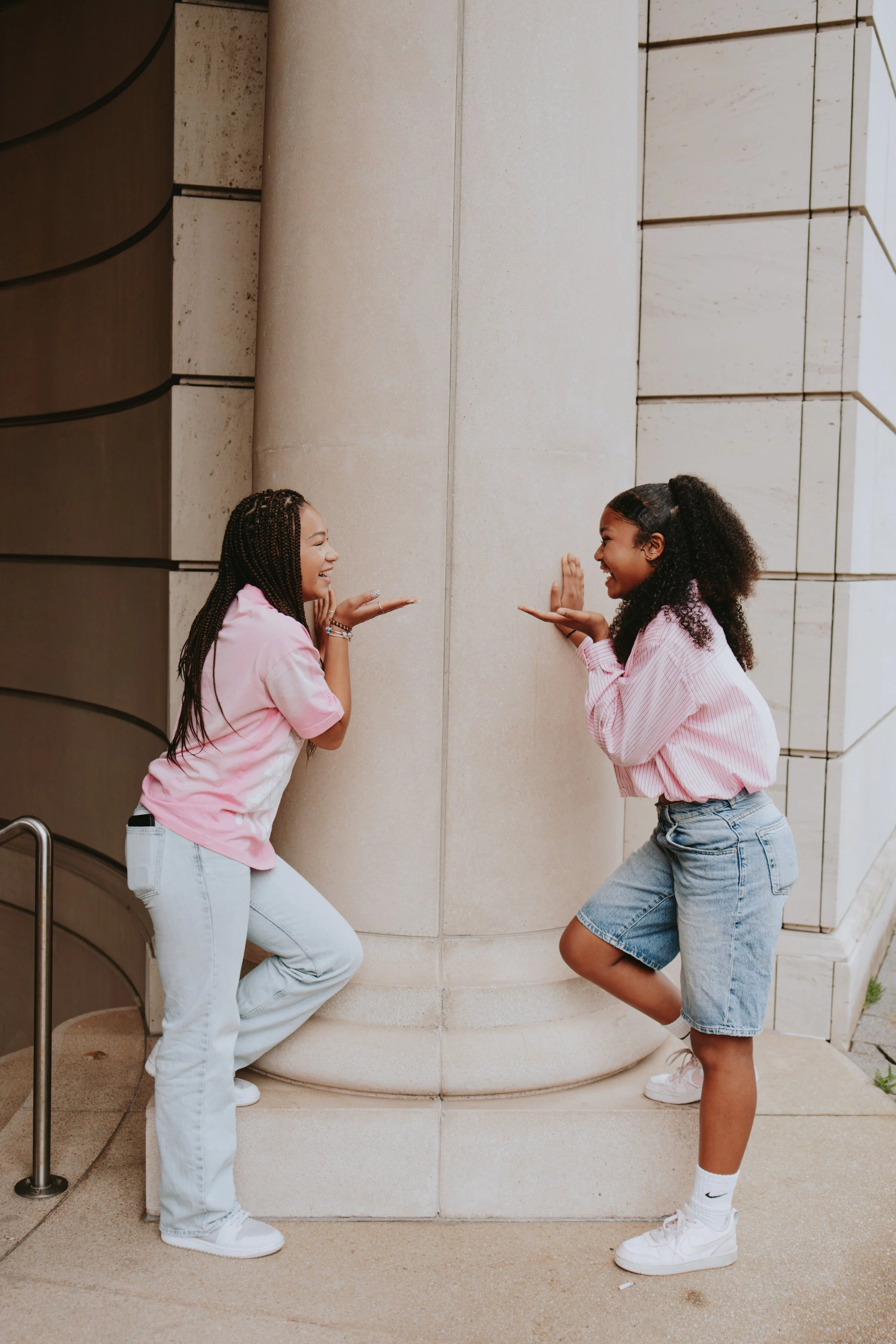 Two women having fun and pretending to push each other against a large stone wall outside. They are smiling and appear to be enjoying each other's company.