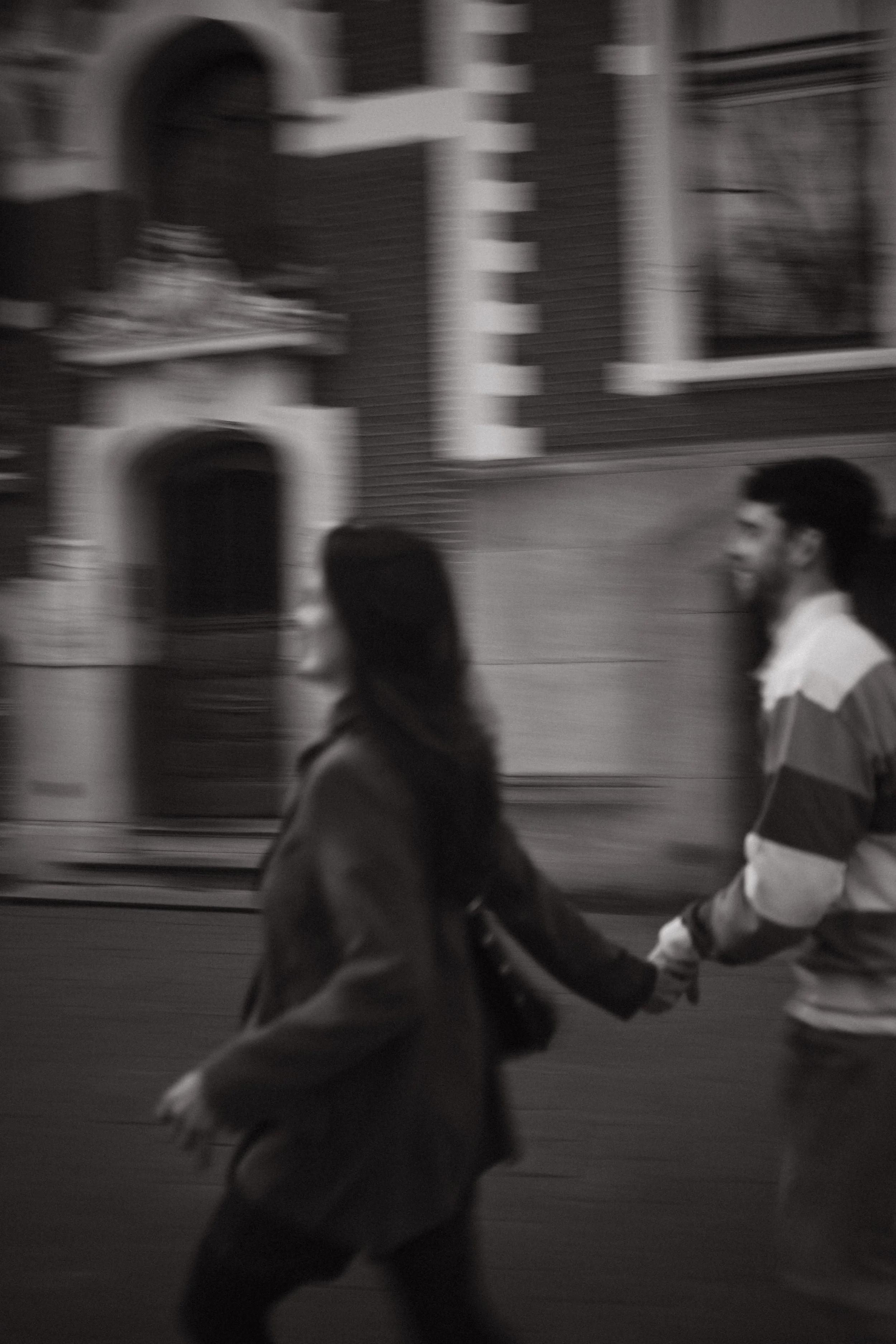 People walking hand in hand outside near a brick building with windows.