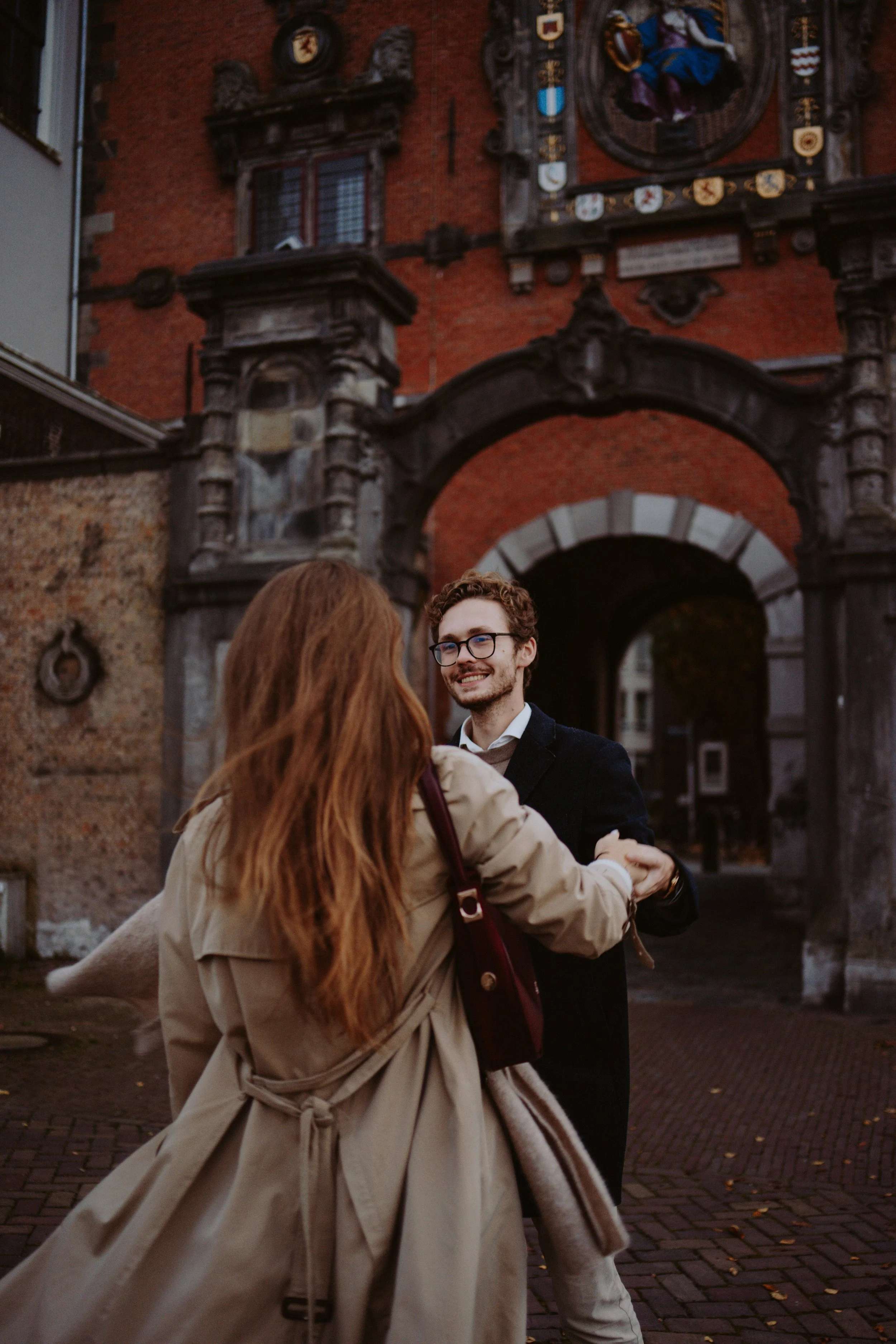 Two people dancing in front of an ornate historical building with coats of arms and a coat of arms with a figure in colorful clothing.