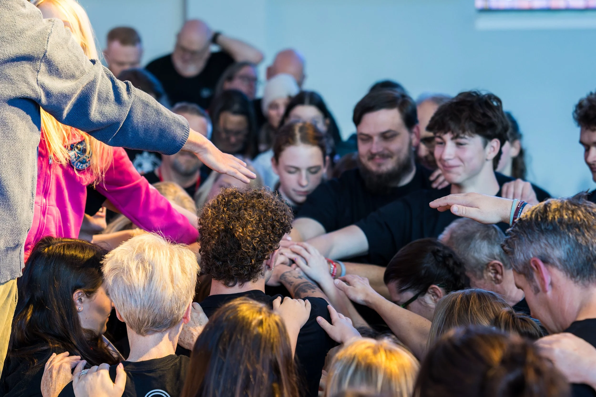 People in a room with their hands stacked in the center, possibly participating in a group activity or ritual.