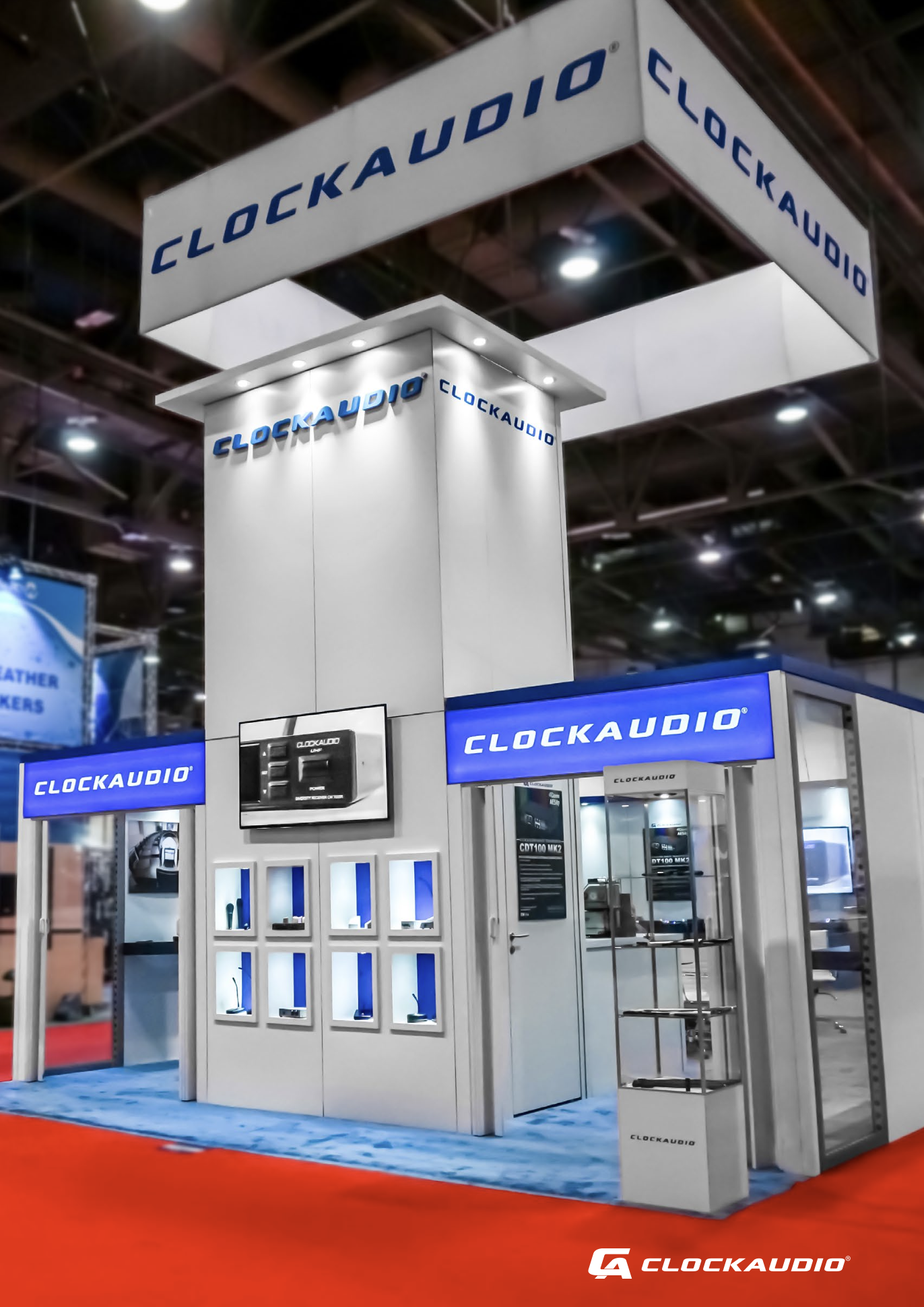 Trade show booth for Clockaudio with displays of audio equipment and products. The booth features a white structure with blue accent lighting and Clockaudio branding. A red carpet surrounds the booth area.