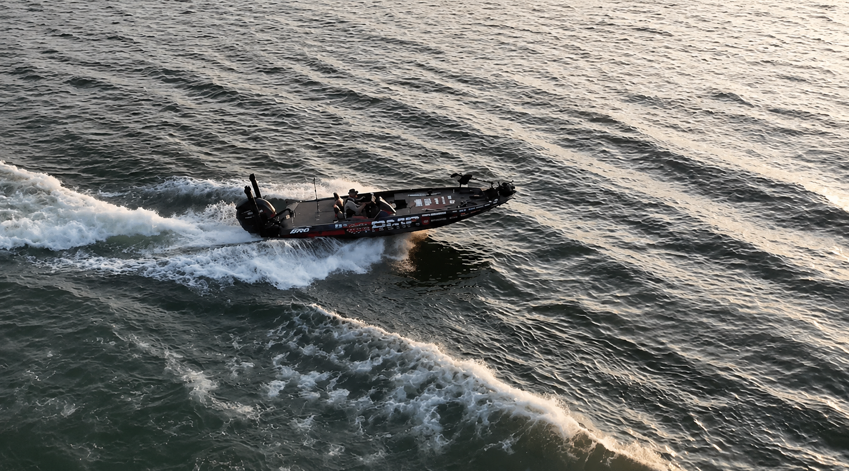 A largemouth bass jumping out of the water during a fishing tournament with a boat in the background and a banner that reads "Lake Oconee Bass Challenge."