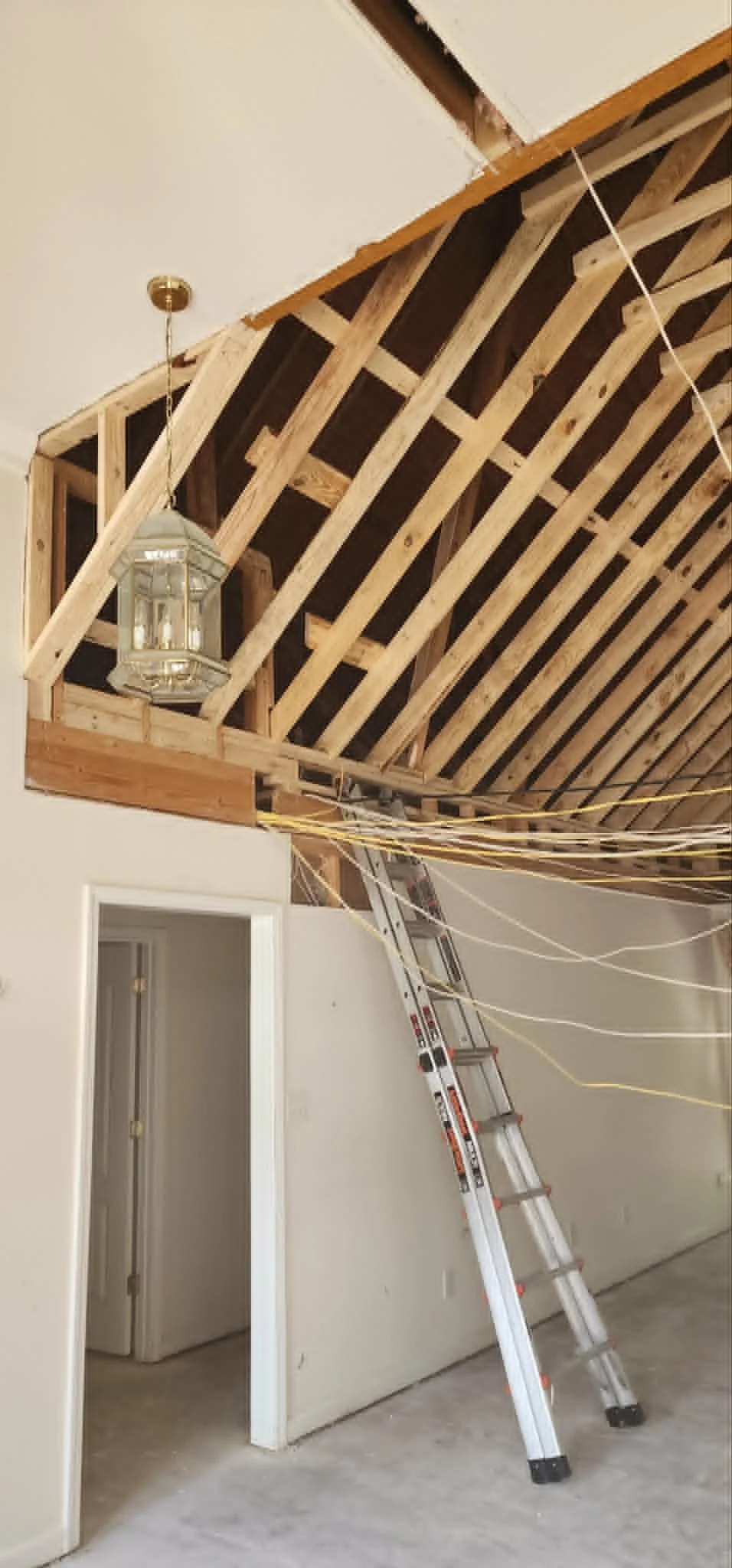 Interior of a room under construction with exposed ceiling framing, a ladder, a hanging lantern, and electrical wiring.