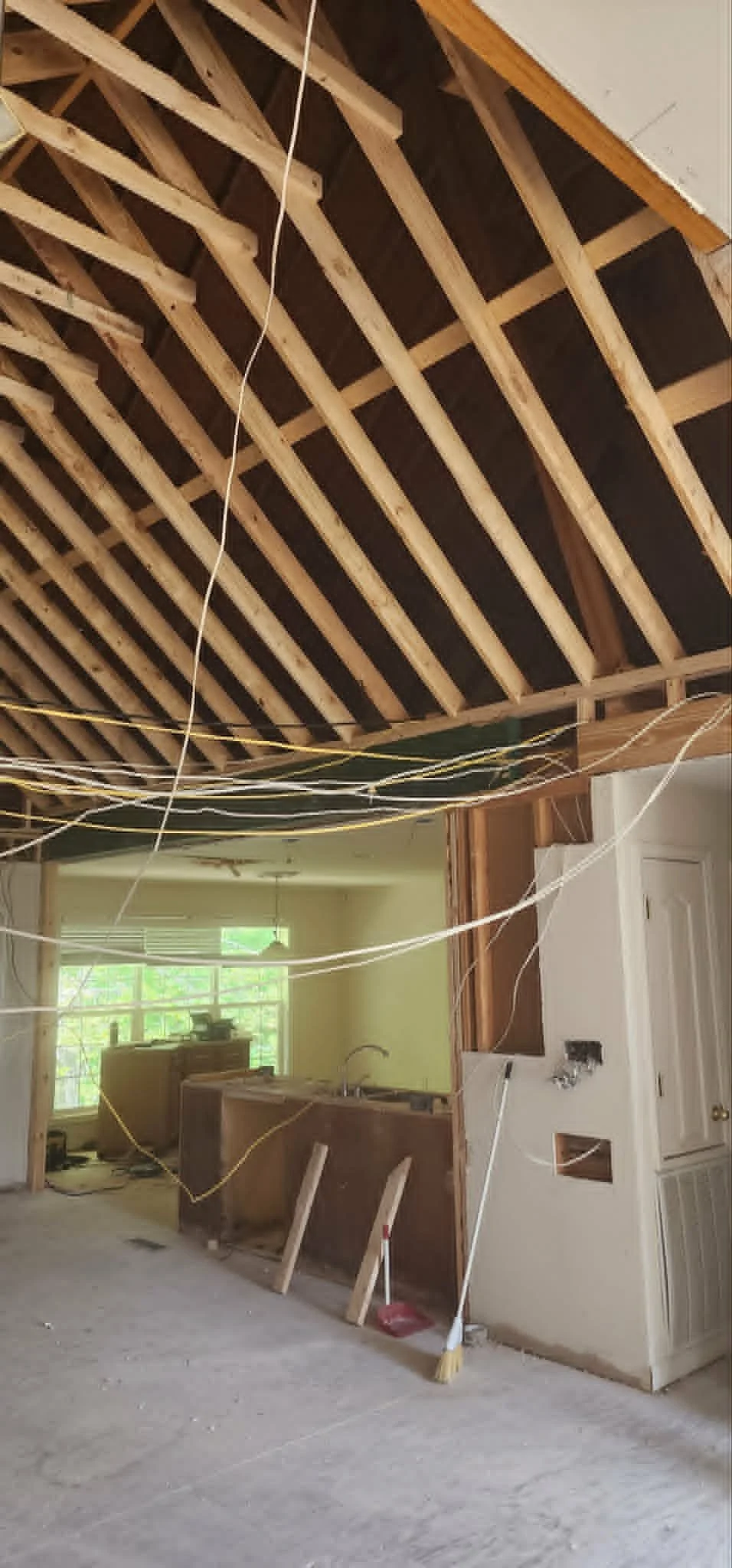 Interior of a room under renovation with exposed wooden ceiling framework, construction wires, and unfinished walls.