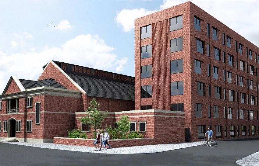A red brick building with a traditional pitched roof and a modern multi-story structure with flat roof and numerous windows, next to a sidewalk with pedestrians and a cyclist.
