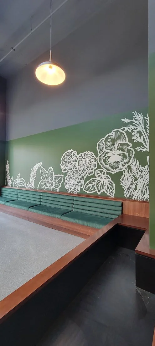 Interior of a waiting area with a green bench against a wall with botanical white chalk drawings.