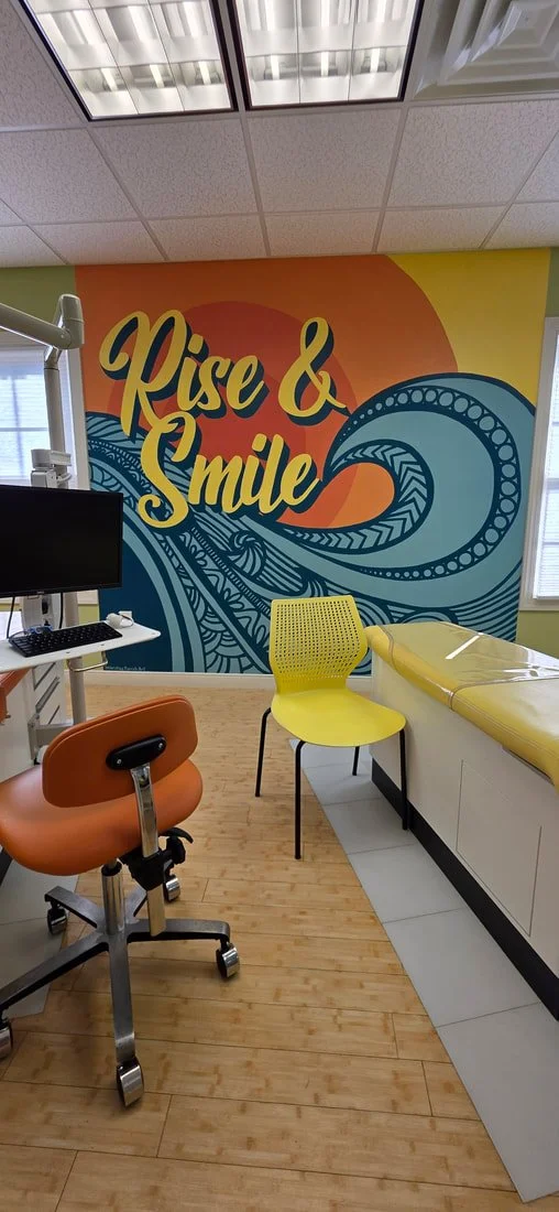 A colorful mural with the words 'Rise & Smile' and artistic wave designs on a wall in a room with medical furniture and equipment.