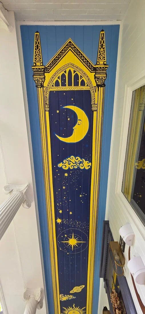 Decorative ceiling mural with celestial themes, including a crescent moon with a face, stars, clouds, a shooting star, and the sun, framed by ornate architectural patterns in gold and blue.