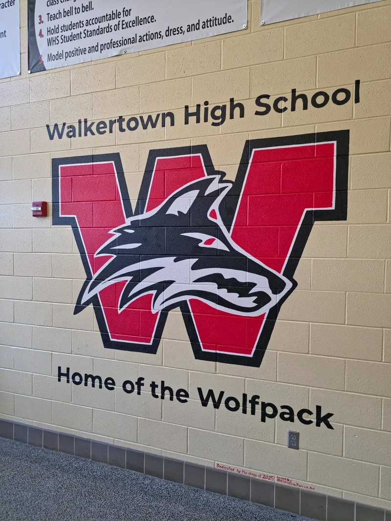 Walkerown High School logo on a beige wall featuring a stylized wolf head inside a red letter 'W', with the text 'Home of the Wolfpack' underneath.