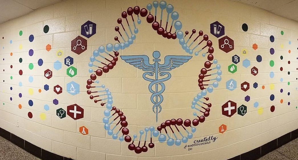 Colorful mural depicting a DNA double helix structure intertwined with a medical caduceus symbol on a school wall, surrounded by various healthcare-themed icons.
