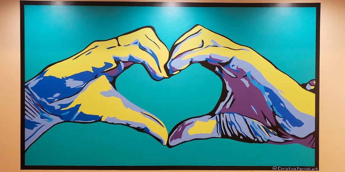A colorful mural of two hands making a heart shape with their fingers on a teal background.