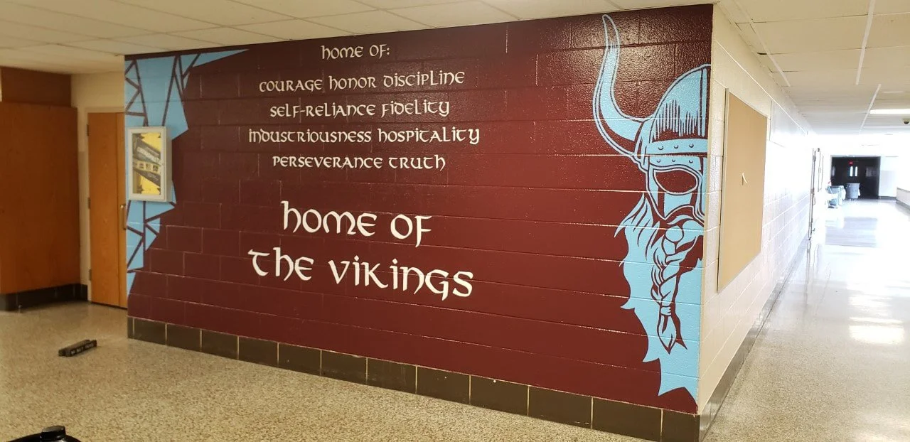 A mural on a school wall with a Viking helmeted warrior illustration and text that reads, "Home of the Vikings," along with a list of qualities: courage, honor, discipline, self-reliance, fidelity, industriousness, hospitality, perseverance, crunch.
