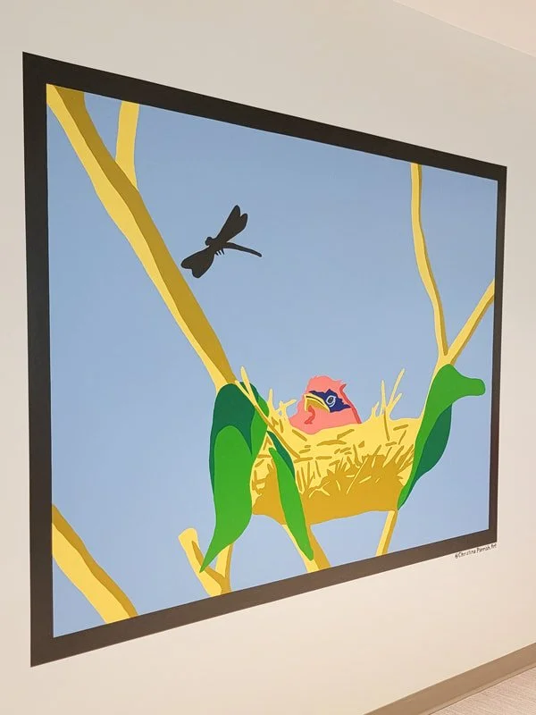A colorful digital illustration of a bird with bright pink feathers and blue markings, sitting in a yellow nest on a tree branch, with a dragonfly flying nearby against a light blue sky background.