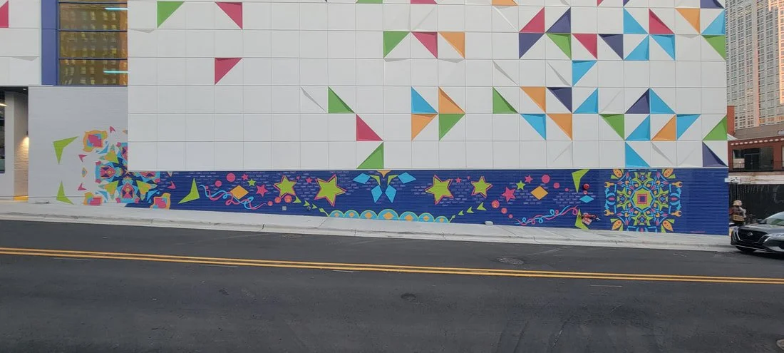 Colorful mural on a building wall with geometric shapes and star patterns, set against a city street with a car passing by.