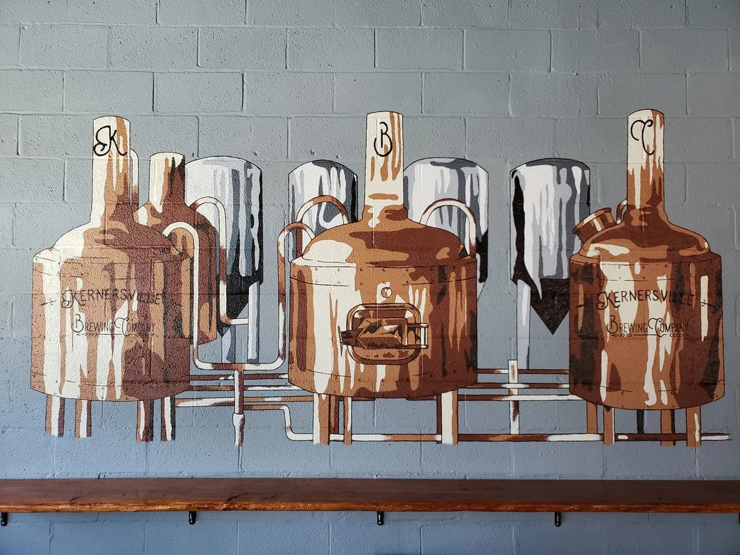 Wall art depicting brewing equipment including copper kettles and metal tanks, with a grey background in a brewery setting.
