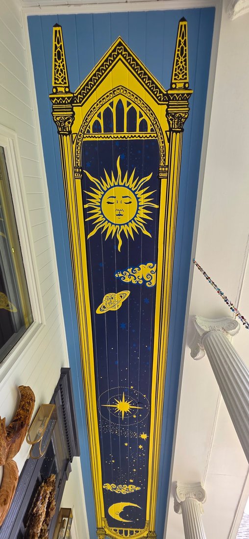 Ceiling mural with celestial designs: a smiling sun, a planet with rings, a star, the moon, and a night sky background, framed by ornate yellow and black architectural elements.