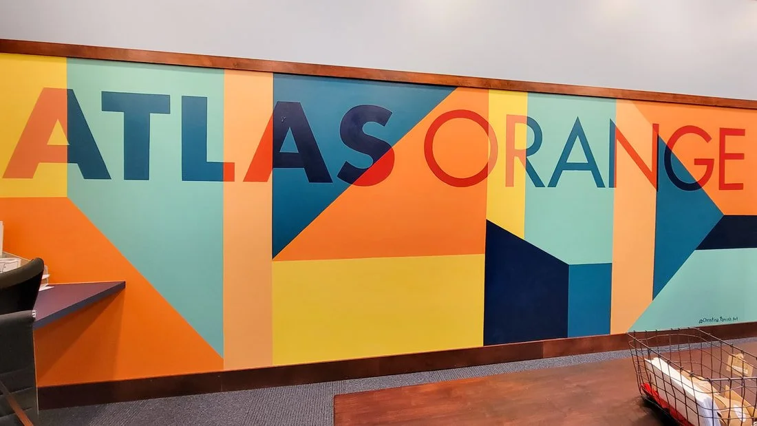 Colorful mural with geometric shapes and the words 'ATLAS ORANGE' on a wall in an office or workspace.