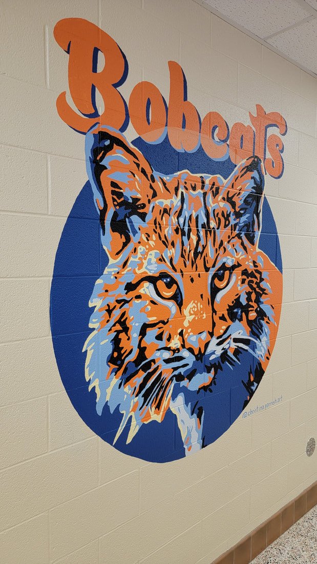 Colorful mural of a bobcat's face with the word 'Bobcats' at the top, painted on a school or gymnasium wall.