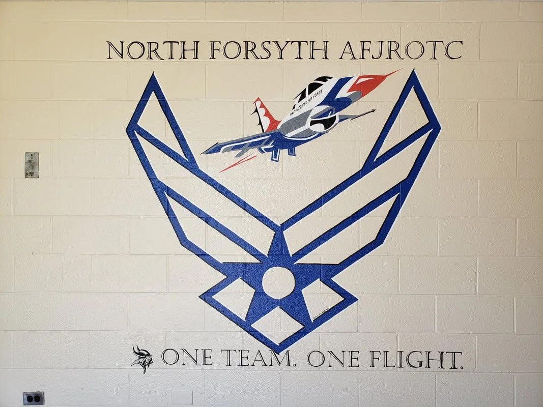 A mural on a wall with the text 'North Forsyth AFJROTC' at the top, a stylized eagle emblem, and a fighter jet graphic above the eagle, with the motto 'One team. One flight.' at the bottom.