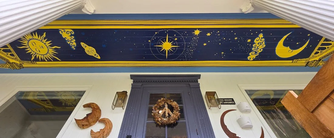 Ceiling mural with sun, planets, stars, and crescent moon, decorated walls with a wreath, wood sculptures, and wall-mounted lights.