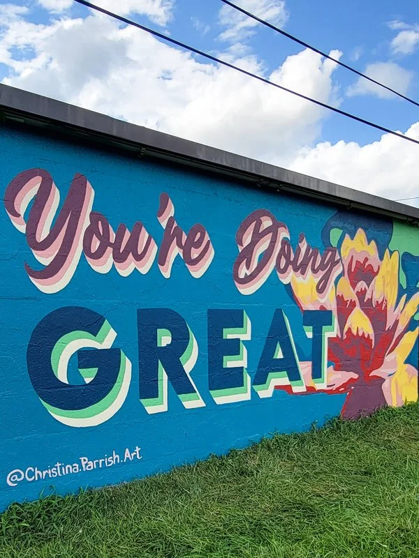Colorful mural on a blue wall with the words 'You're Doing GREAT' and a large multicolored flower