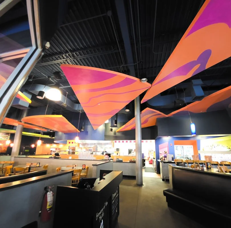 Interior of a restaurant with vibrant orange and purple fabric ceiling decor, yellow chairs, and a brightly lit counter area.