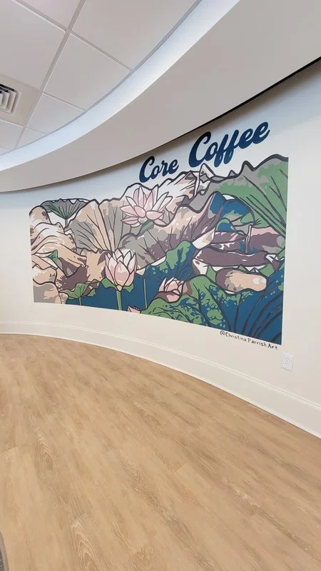 Colorful mural of mountains, mountains, a river, and lotus flowers with the words "Core Coffee" on a white wall in a modern interior space.