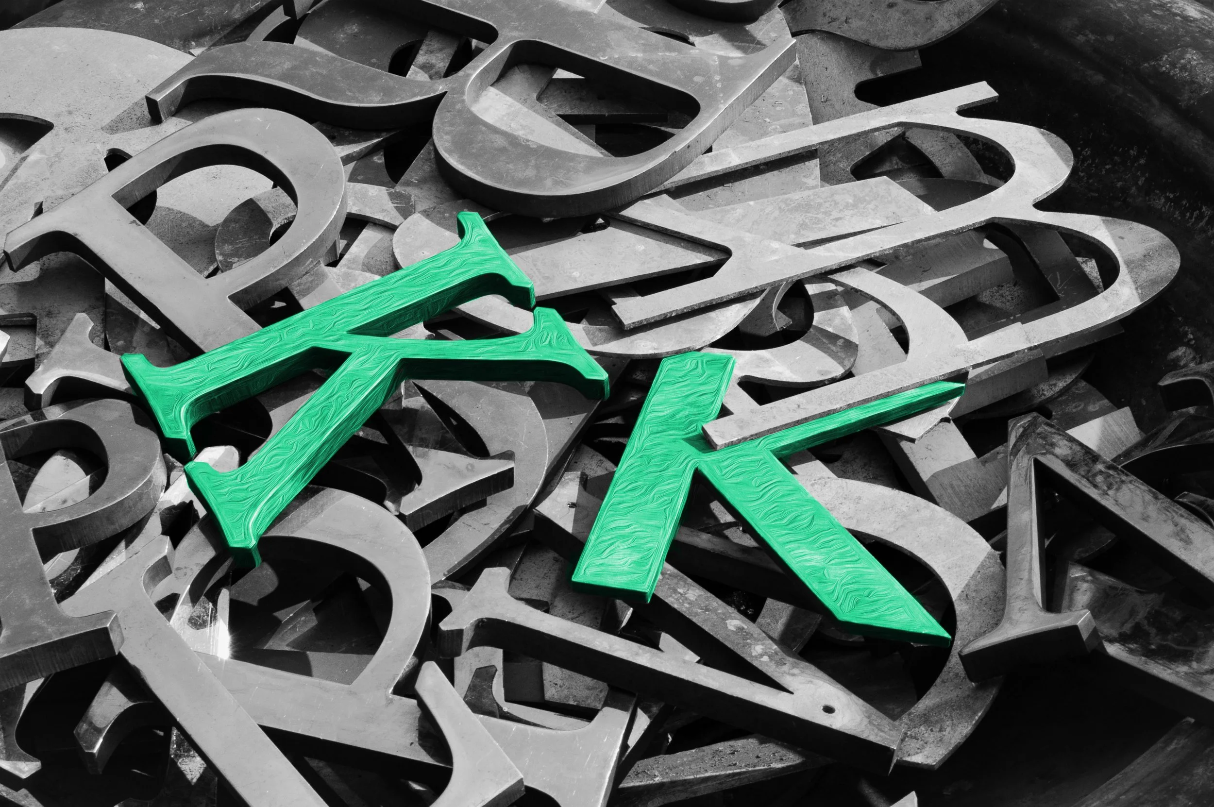 Pile of mixed metal letters with two green letter K's in the center