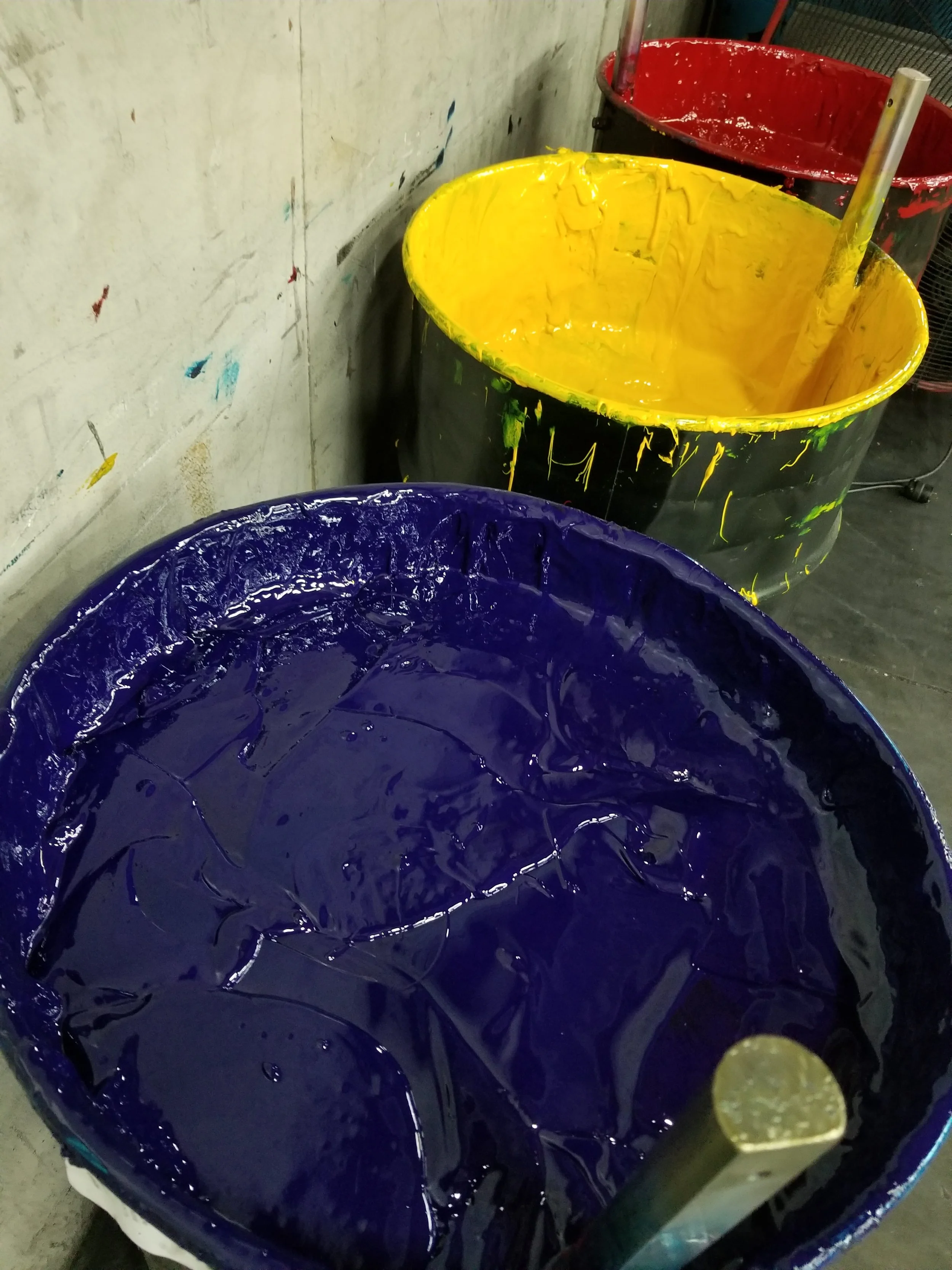 Buckets of paint in purple, yellow, and red arranged in a workshop.