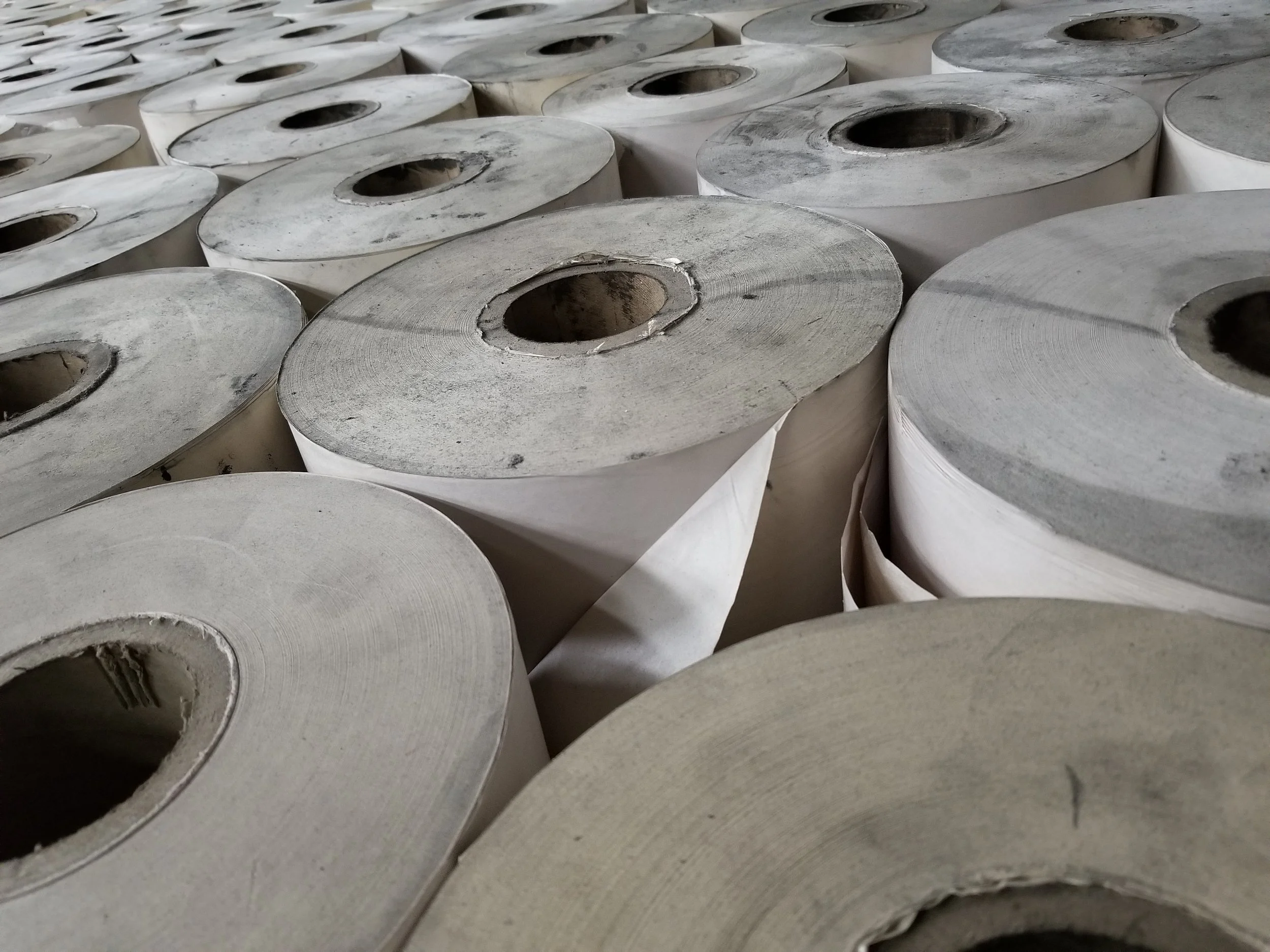 Rows of large industrial paper rolls stacked in a warehouse.