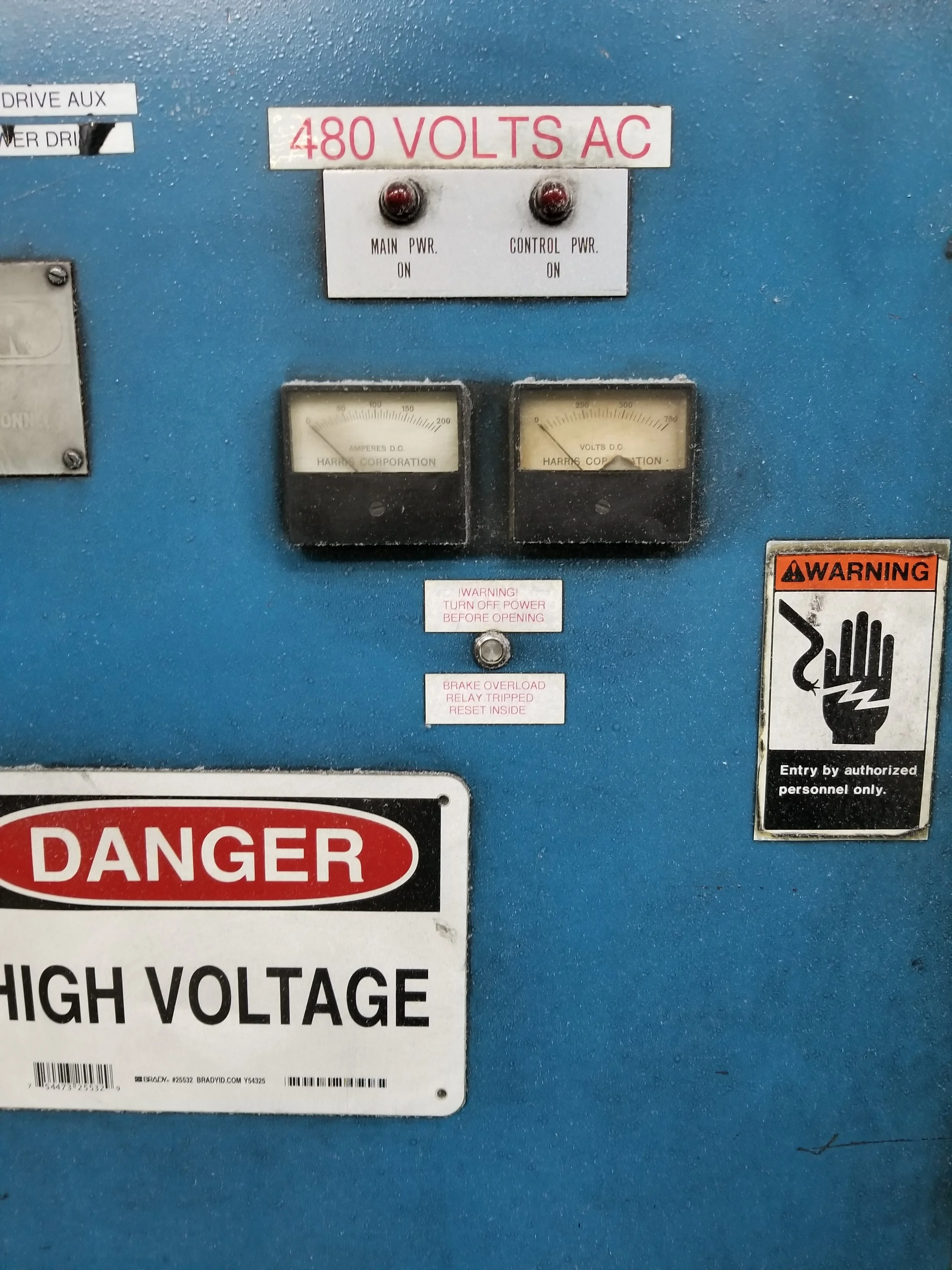 Electrical control panel with 480 volts AC warning, ammeter and voltmeter gauges, and high voltage danger signs.