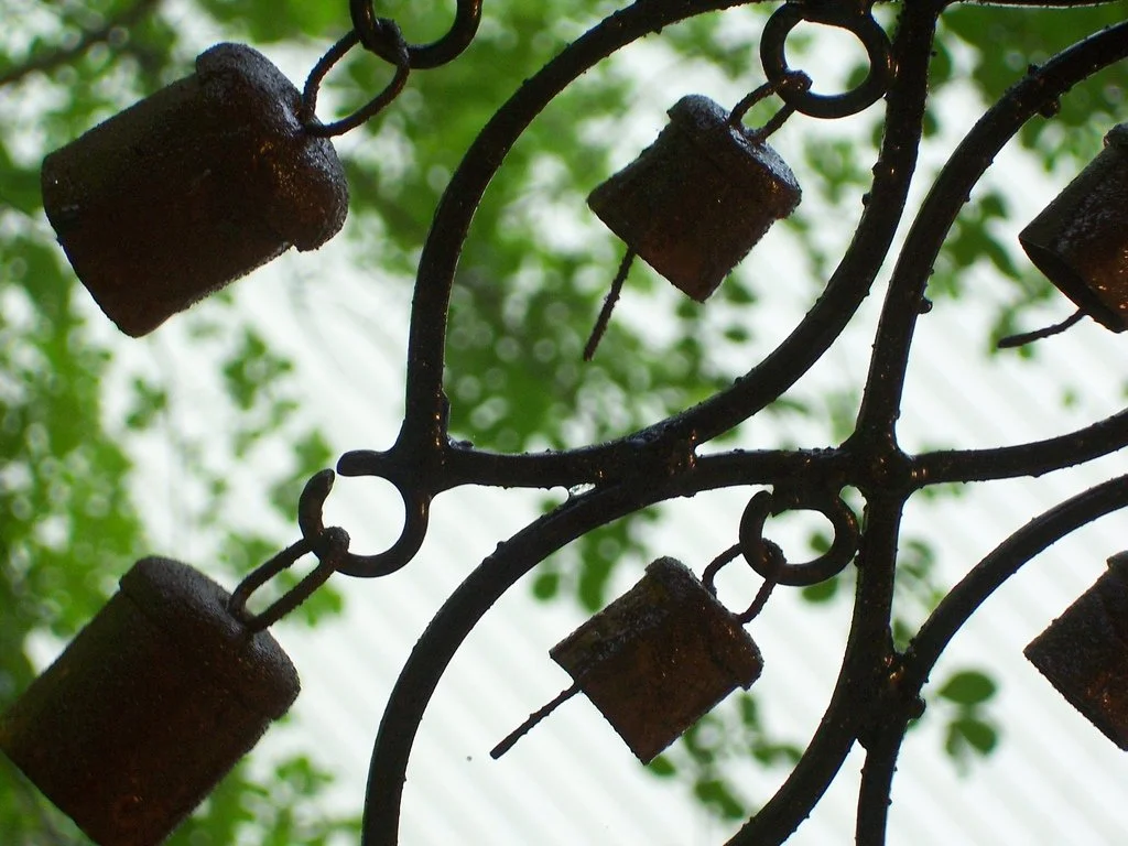 Close-up of a metal wind chime with green foliage in the background.