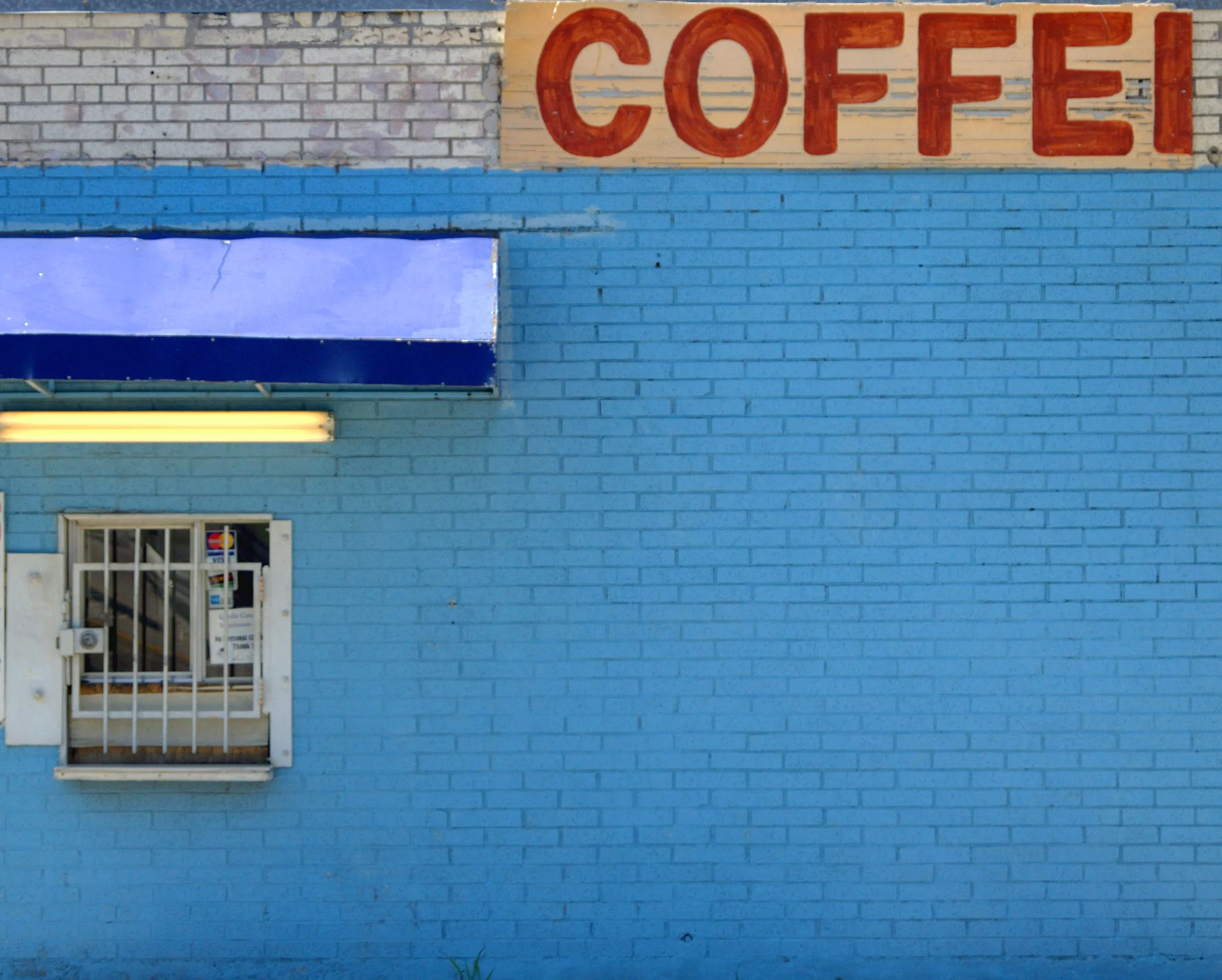 Blue brick wall with 'COFFEE' partially visible, featuring a small barred window and blue awning.