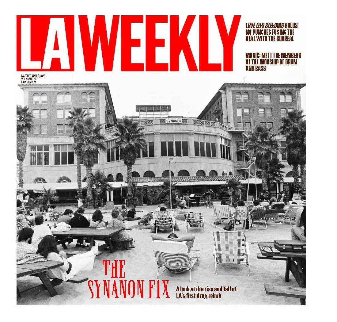 Cover of LA Weekly magazine showing a black-and-white photo of a public outdoor space with people sitting, lounging, and enjoying live music. The background features a multi-story building with palm trees in front. The magazine title "LA Weekly" is in large red letters at the top, and other headlines are in smaller brown and red text.