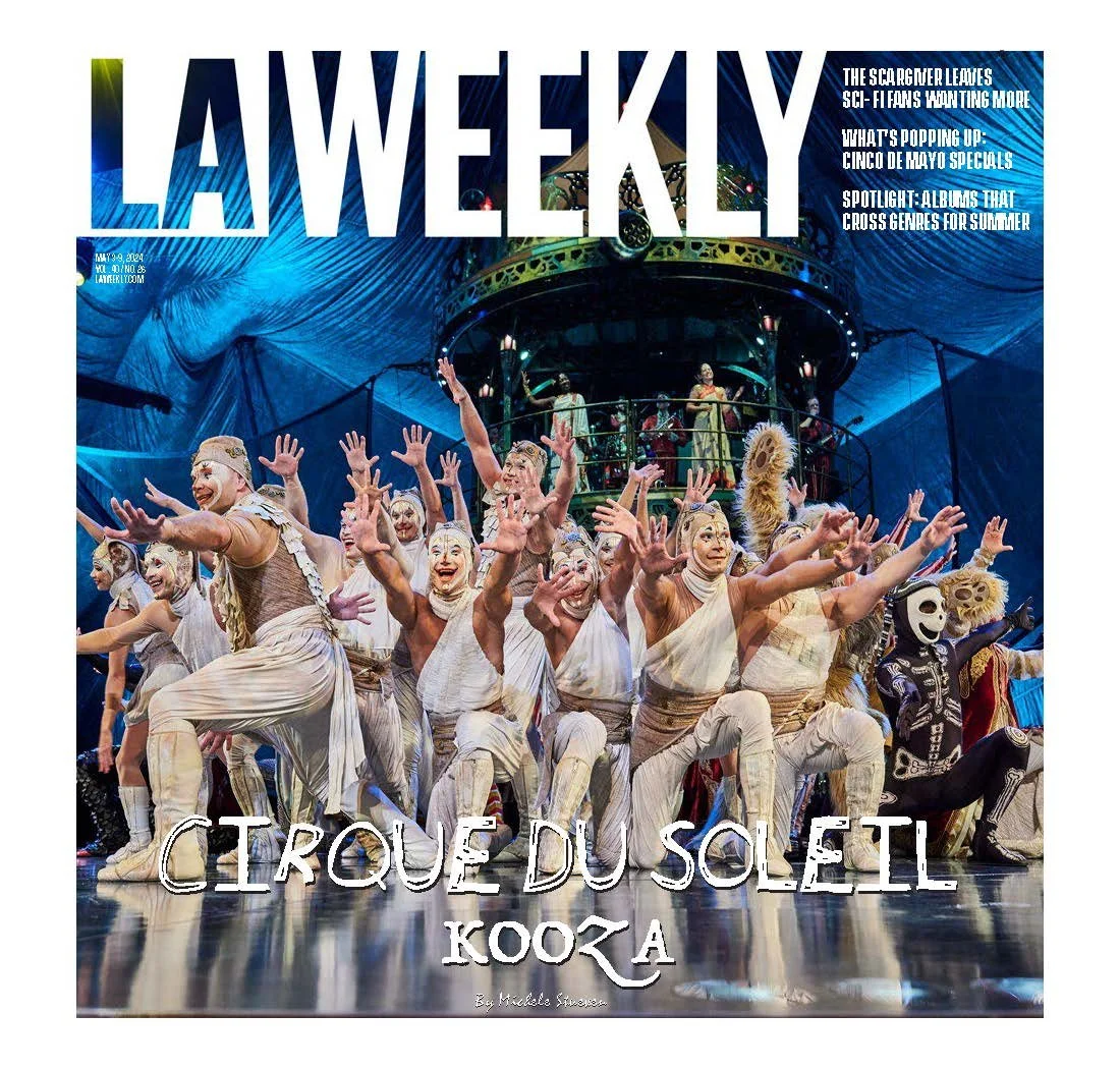 Cover of LA Weekly magazine featuring a stage performance by Cirque du Soleil Kooza with performers in colorful costumes and masks, with a blue backdrop and a circular structure in the background.