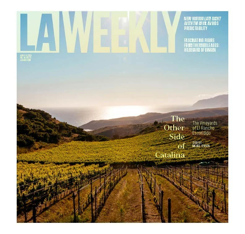 Cover of LA Weekly magazine featuring a vineyard landscape with rows of grapevines, green hills, and an ocean in the background under a clear sky.