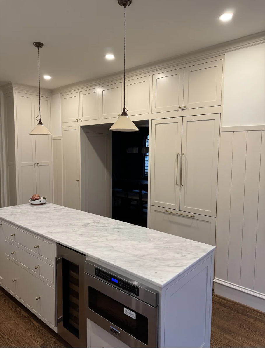 Modern kitchen with white cabinets, marble island, built-in wine cooler, microwave, and pendant lights.