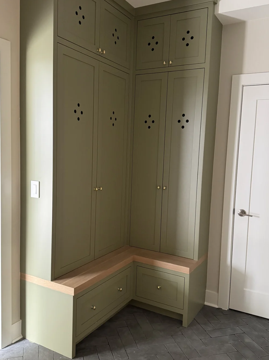 Corner of a room with green built-in cabinets with small round knobs, a wooden bench with drawers beneath, and a white door.