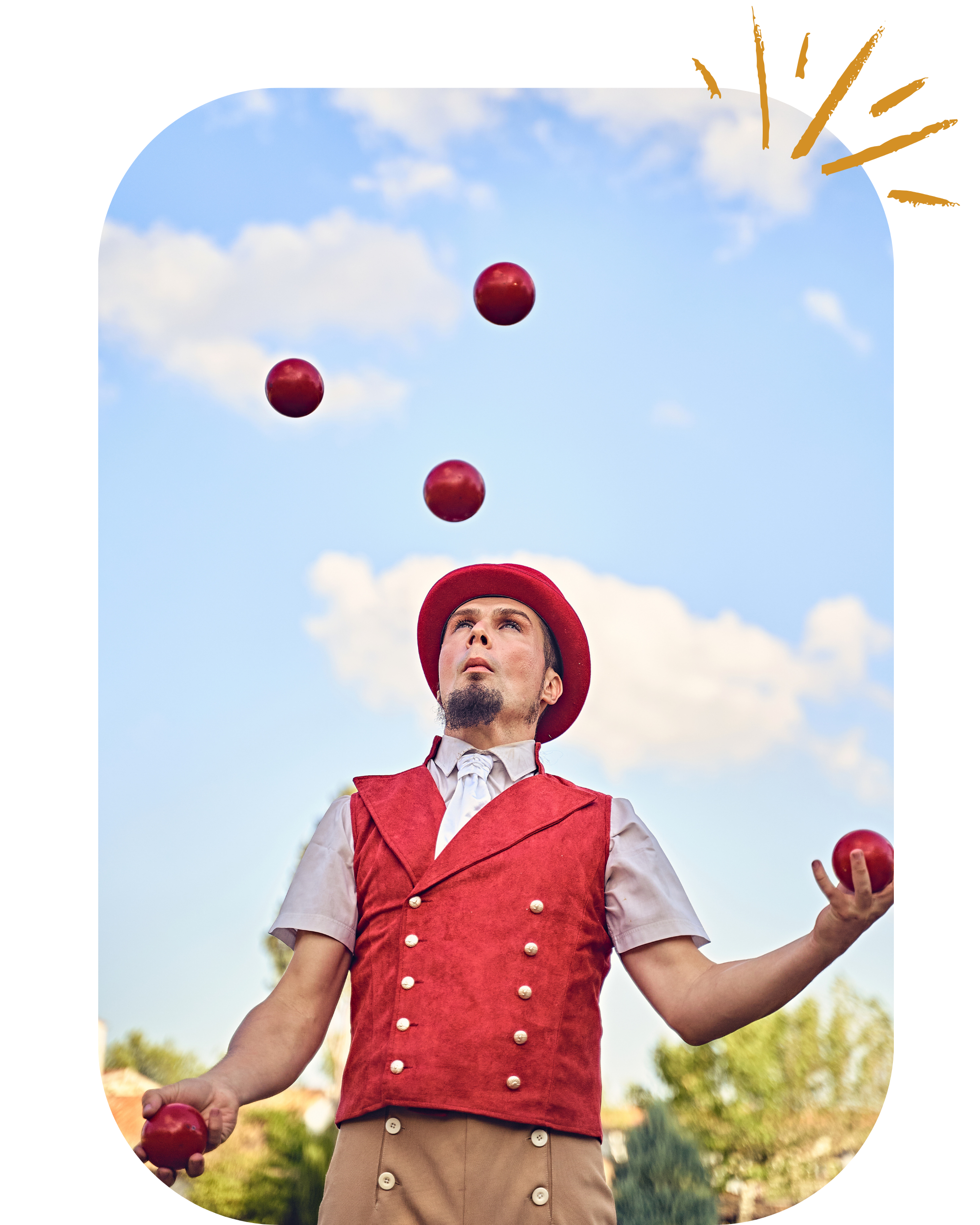 A person dressed in vintage clown attire, including a red vest with gold buttons, a white shirt, beige pants with buttons, and a red hat with a white pom-pom, juggles three red balls outdoors under a blue sky with clouds.