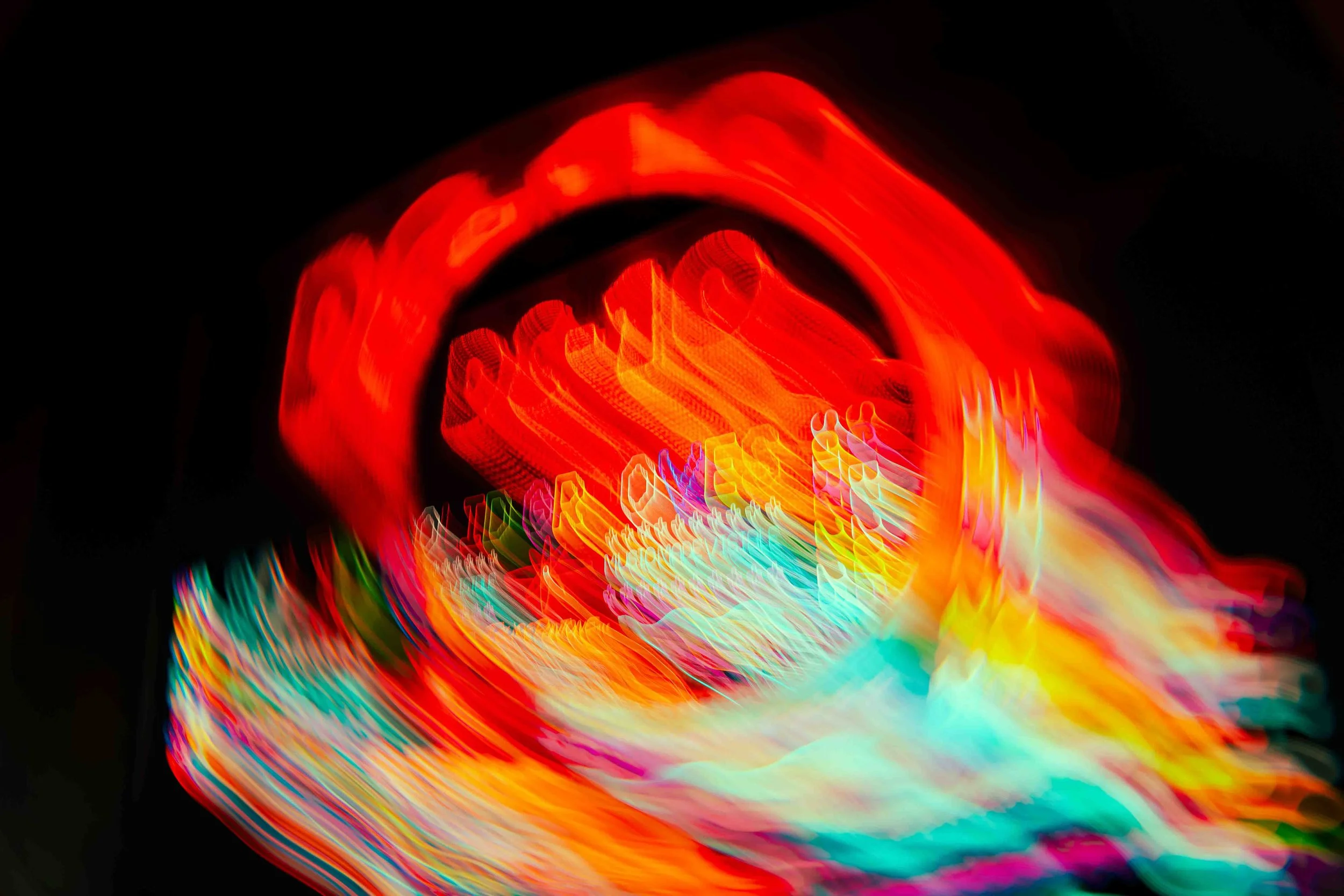 Abstract vibrant neon light trails in red, yellow, blue, green, and purple against a black background, creating a dynamic and colorful visual effect.