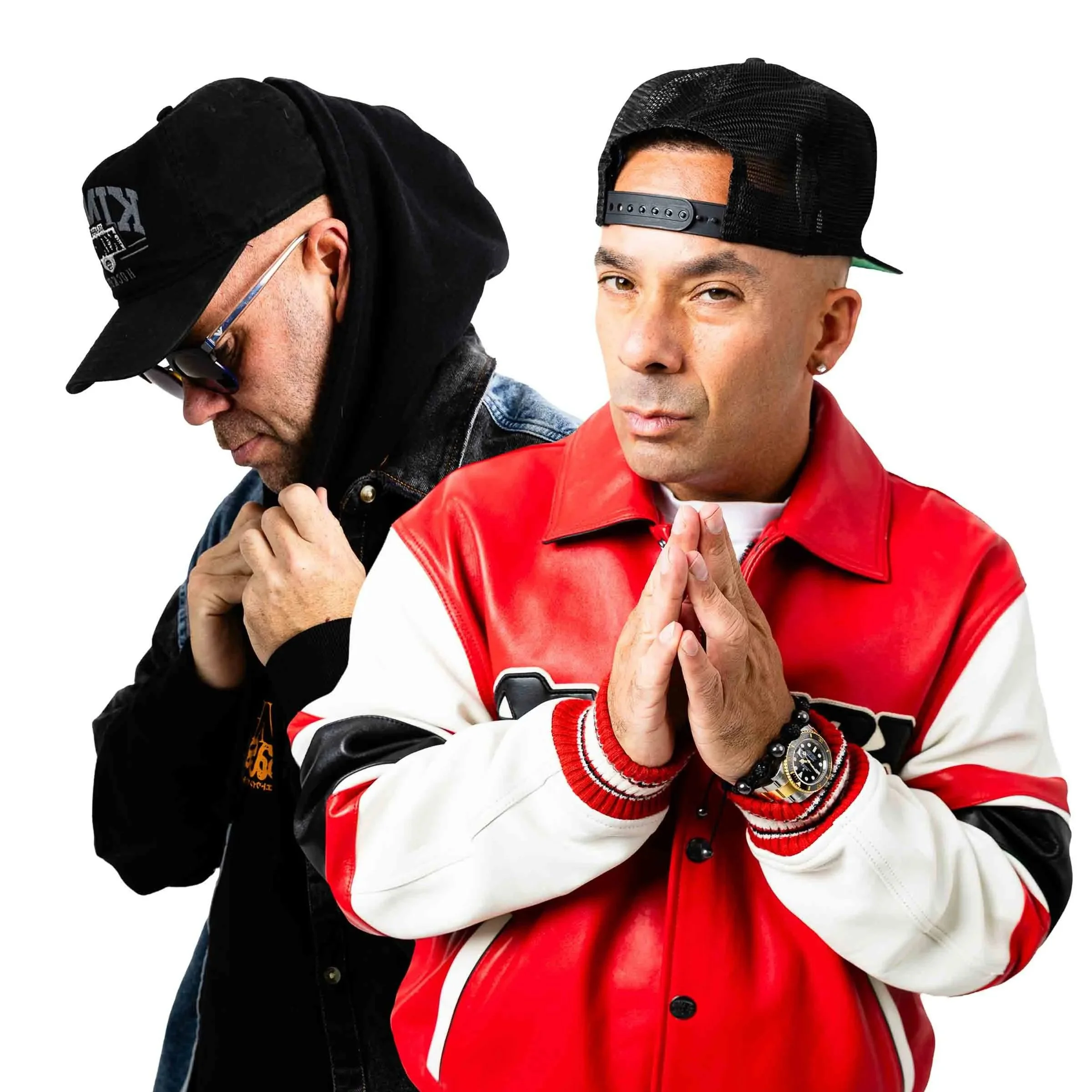 Solardo wearing baseball caps and jackets, one with a red and white jacket and pressed hands, the other with a black hoodie and cap, against a white background.