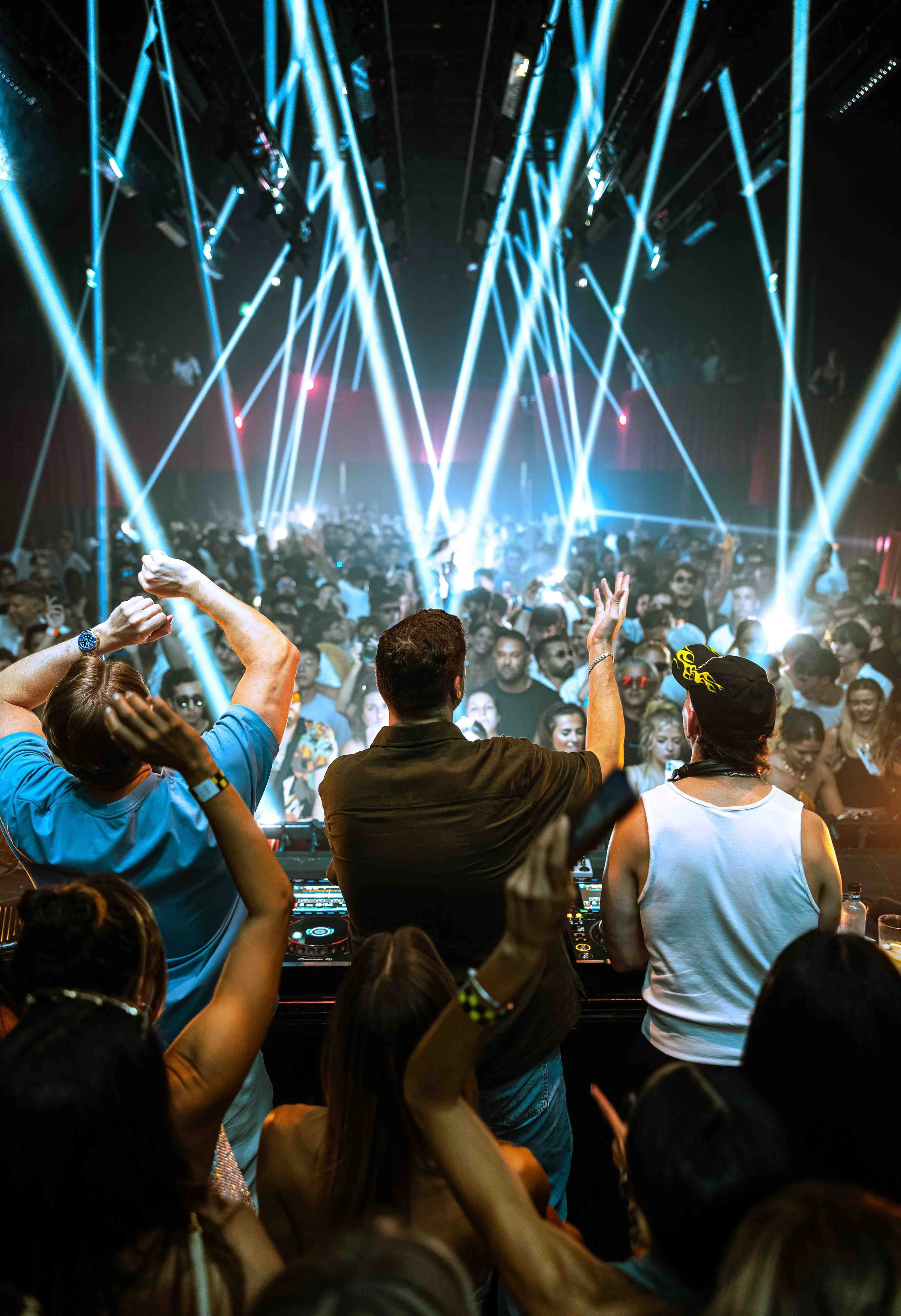 Crowd dancing and enjoying a concert or music event with bright blue laser lights overhead.