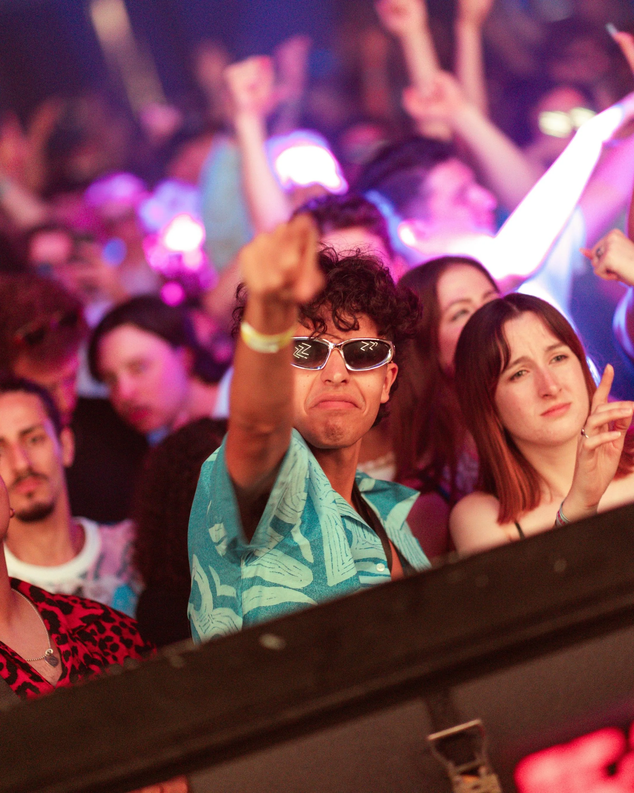 People at a concert or party dancing and enjoying music with one person wearing sunglasses and a tropical shirt in the foreground.