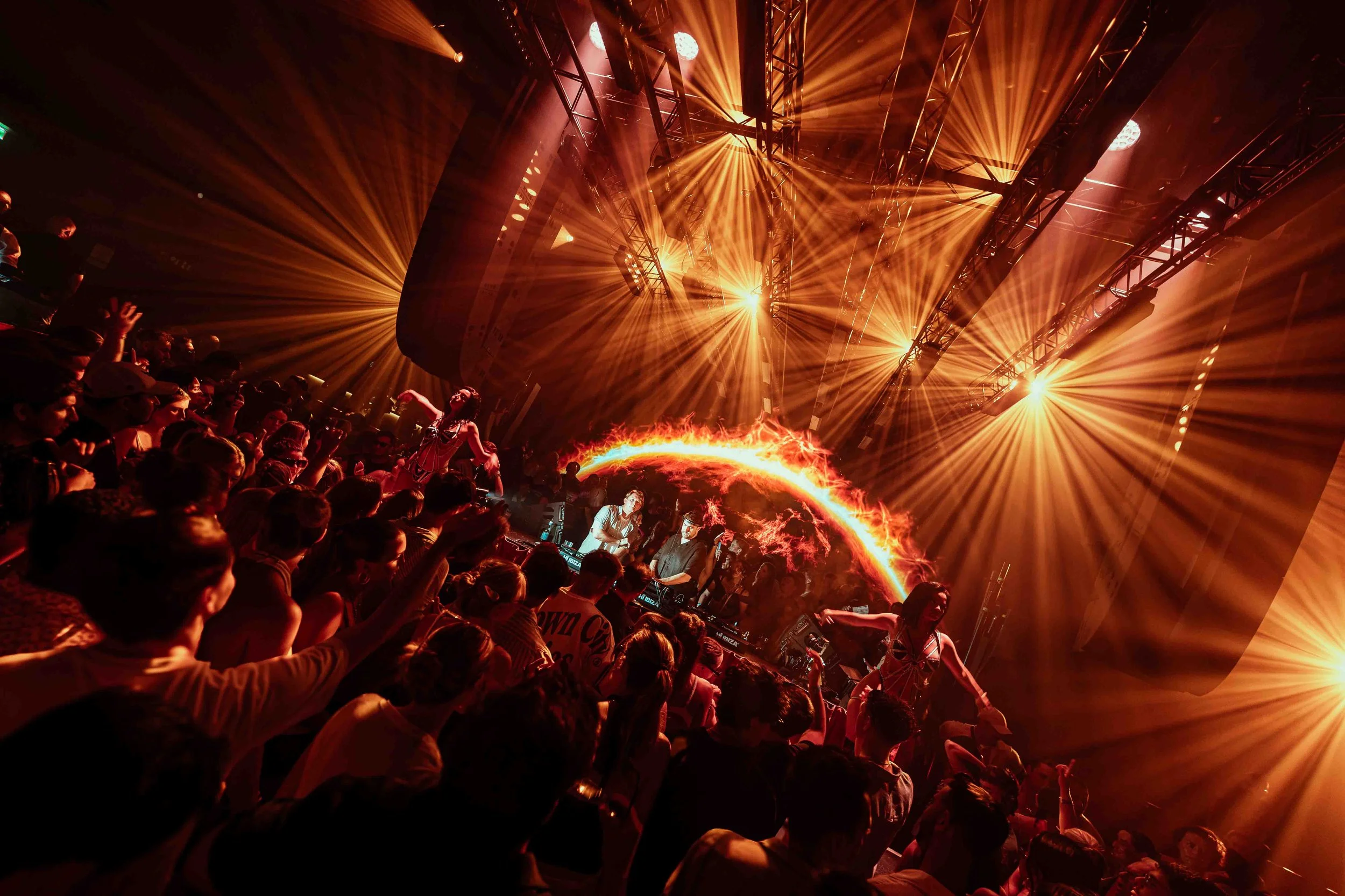 Crowd of people at a music concert with vibrant orange stage lighting and laser effects.