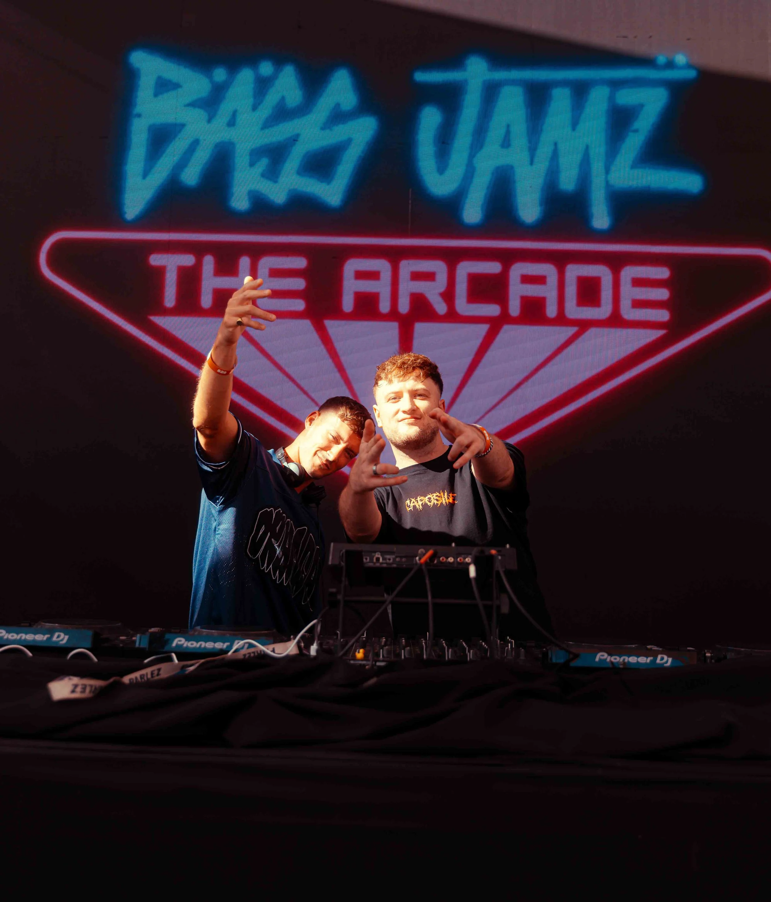 Fans at the Zowie The Arcade event, with two young men making hand gestures in front of a large neon sign that reads "Zowie The Arcade."